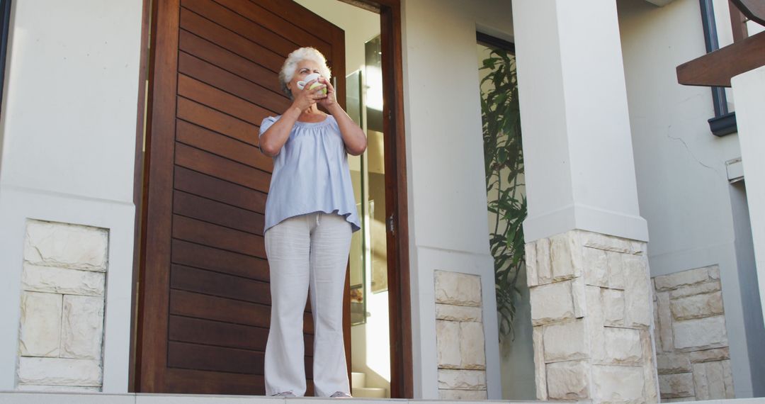 African american senior woman drinking coffee while standing at the front door at home - Free Images, Stock Photos and Pictures on Pikwizard.com