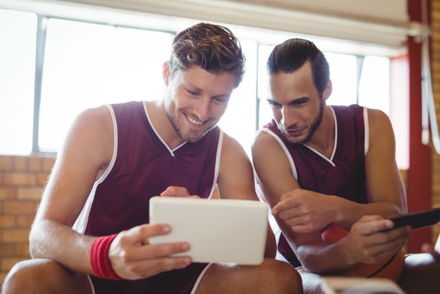 Smiling basketball players talking while using digital tablet in the court
