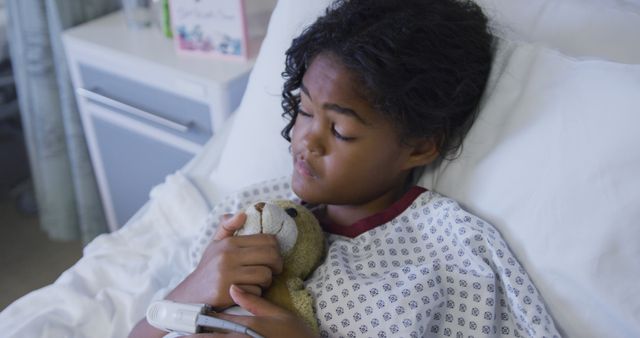 Mixed race girl lying on hospital bed wearing fingertip pulse oximeter and holding teddy bear. medicine, health and healthcare services.