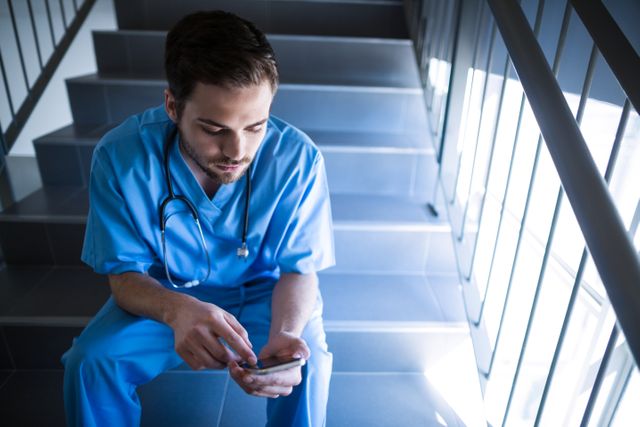Male nurse sitting on staircase and using mobile phone - Download Free Stock Photos Pikwizard.com