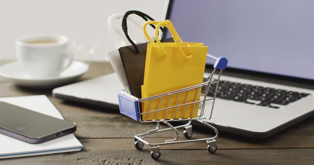 Gift bags in shopping trolley on desk with smartphone and laptop. Global business, online shopping, cyber monday, sale and retail concept digitally generated image.
