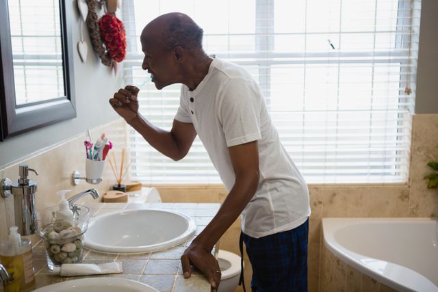 Side view of senior man brushing teeth by sink in bathroom at home