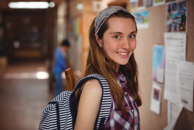 Portrait of smiling schoolgirl standing near notice board in corridor - Download Free Stock Photos Pikwizard.com