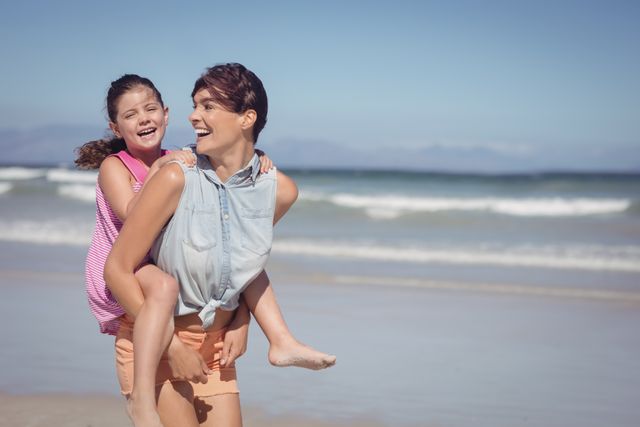 Cheerful mother piggybacking daughter at beach - Download Free Stock Photos Pikwizard.com