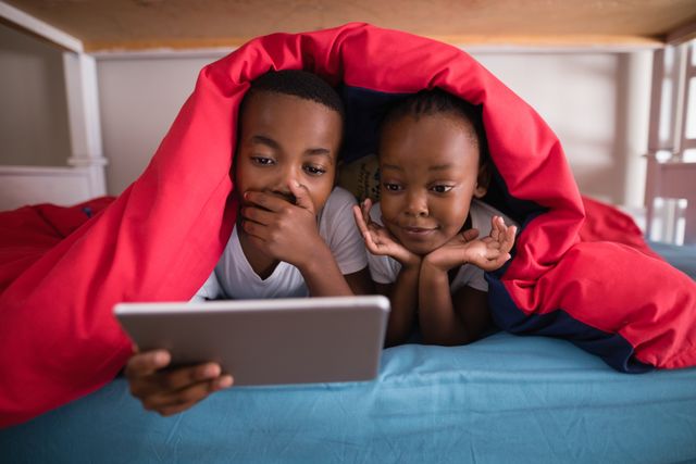Surprised siblings holding digital tablet while lying on bed - Download Free Stock Photos Pikwizard.com