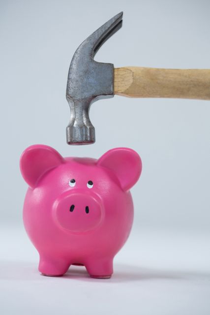Piggy bank about to be smashed by hammer on white background