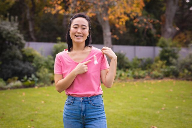 Smiling asian woman in pink tshirt showing pink bow to camera. healthcare, medicine, cancer awareness sign.