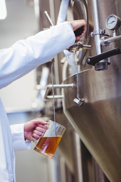 Cropped image of manufacturer filling beer into glass at brewery