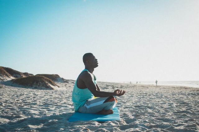 African american man exercising, practicing yoga, meditating on beach at sunset - Download Free Stock Photos Pikwizard.com