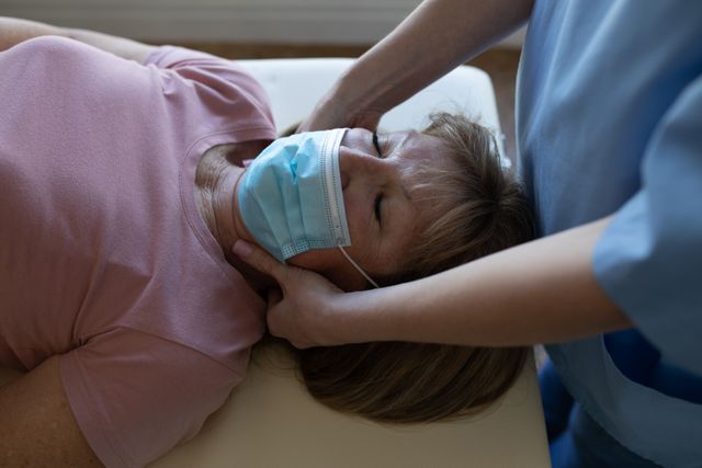Female health worker massaging neck of senior woman wearing face mask - Download Free Stock Photos Pikwizard.com