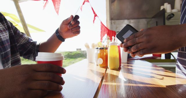 Midsection of african american man paying male owner for coffee by credit card at food truck. small independent business, street food, service and catering.
