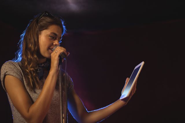 Confident female singer holding digital tablet while performing at music concert - Download Free Stock Photos Pikwizard.com