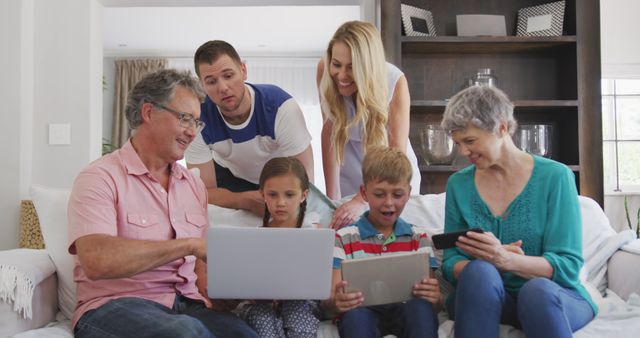 Happy caucasian family sitting on sofa in living room, using laptop, tablet and smartphone. Lifestyle, domestic life, communication, family, and togetherness.