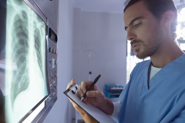 Male surgeon writing on clipboard while examining x-ray on x-ray light box in operation room - Download Free Stock Photos Pikwizard.com