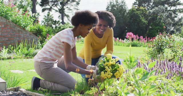 Portrait of smiling african american mother and daughter gardening together in sunny garden. domestic life and quality family time together at home.