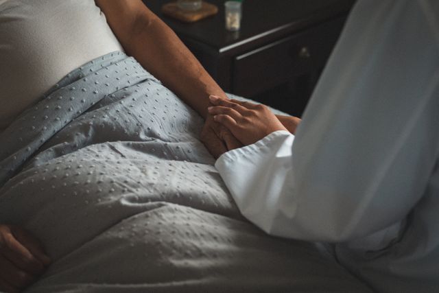Midsection of senior mixed race man lying in bed holding hands with medical worker - Download Free Stock Photos Pikwizard.com