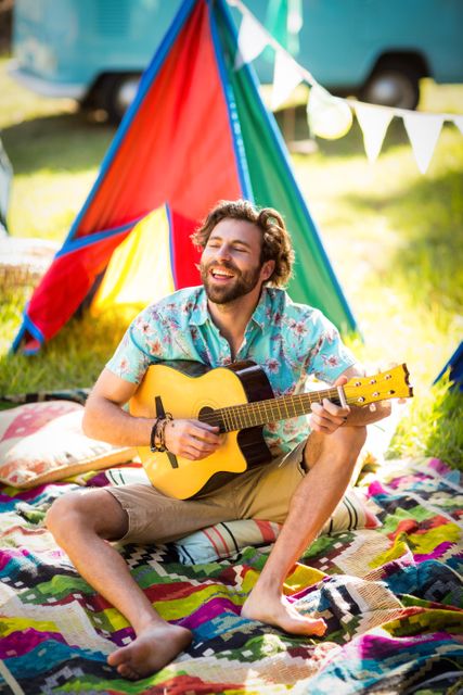 Man playing guitar at campsite in park on a sunny day