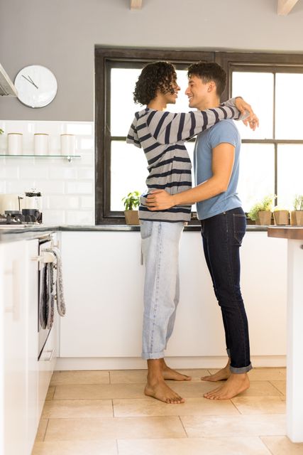 Loving multiracial young gay couple looking at each other and smiling while embracing in kitchen. Copy space, happy, romance, unaltered, love, togetherness, homosexual, lifestyle and home concept.