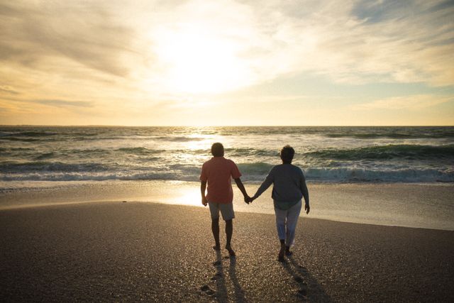 Full length of senior couple holding hands while walking towards shore at beach during sunset. lifestyle, love and weekend.