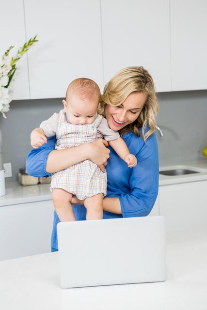 Mother and baby boy using laptop in kitchen - Download Free Stock Photos Pikwizard.com