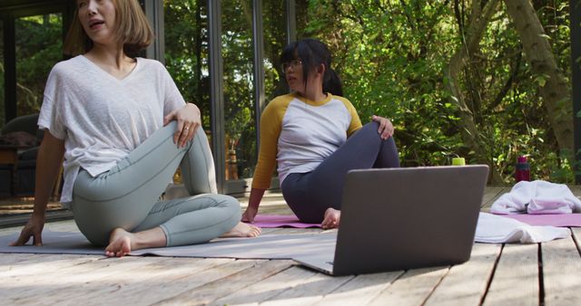 Asian mother and daughter practicing yoga outdoors in garden with laptop. at home in isolation during quarantine lockdown.
