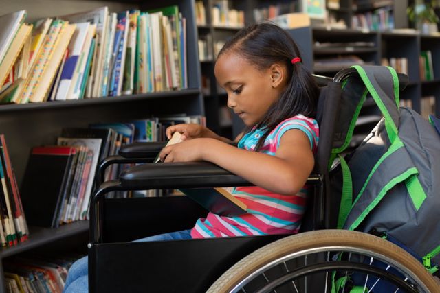 Side view of a cute disabled mixed-race schoolgirl reading a book in the classroom at school