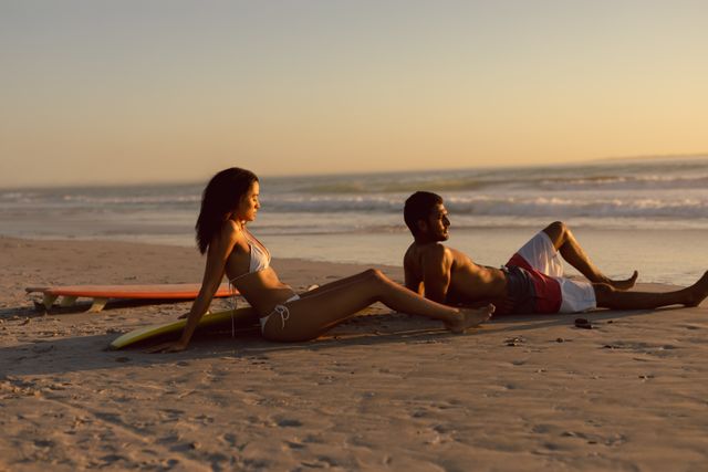 Couple with surfboard relaxing on the beach at dusk - Download Free Stock Photos Pikwizard.com