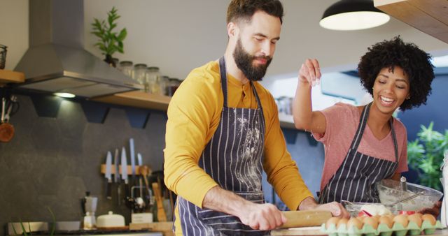Image of happy diverse couple in aprons talking and baking together in kitchen, with copy space. Happiness, inclusivity, free time, togetherness and domestic life.