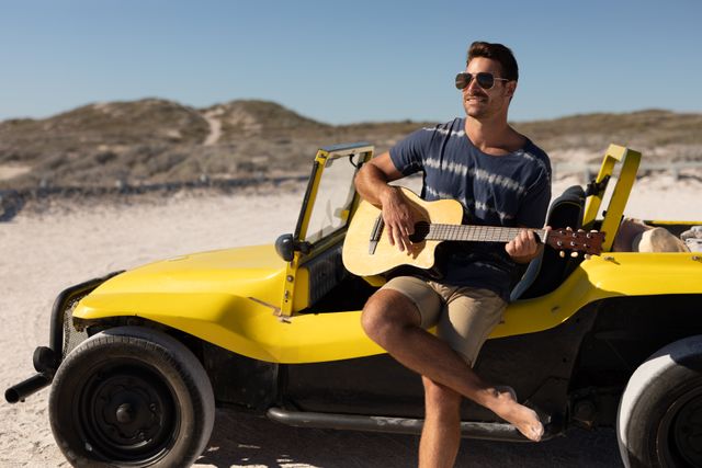 Smiling caucasian man in sunglasses sitting on beach buggy playing guitar on sunny beach - Download Free Stock Photos Pikwizard.com