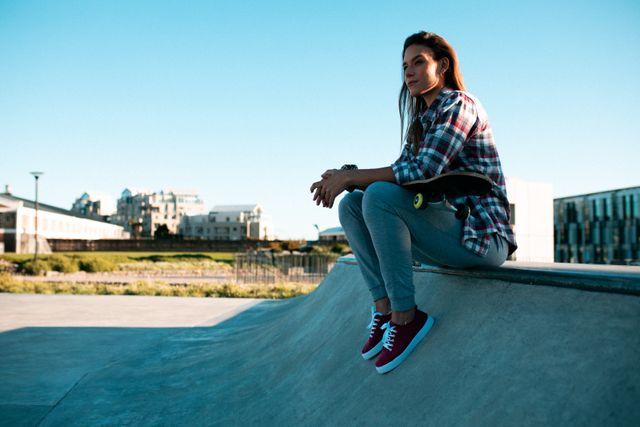 Portrait of caucasian woman sitting on wall at skatepark in the sun - Download Free Stock Photos Pikwizard.com