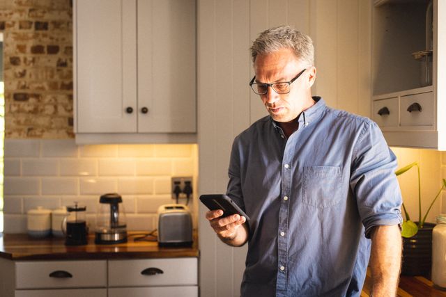 Caucasian man wearing glasses and using smartphone in kitchen - Download Free Stock Photos Pikwizard.com
