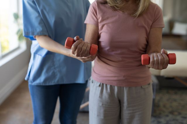 Mid section of female health worker assisting senior woman to exercise with dumbbells at home - Download Free Stock Photos Pikwizard.com