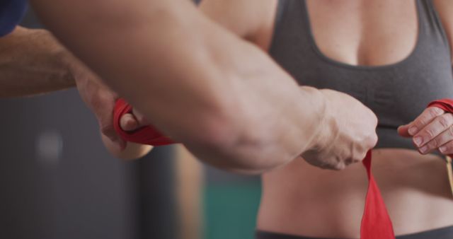 Mid section of male trainer wrapping boxing tape on hands of female boxer at the gym. sports, training and fitness concept