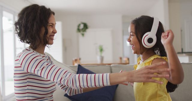 Happy hispanic mother and daughter wearing headphones listening to music sitting on sofa. at home in isolation during quarantine lockdown.