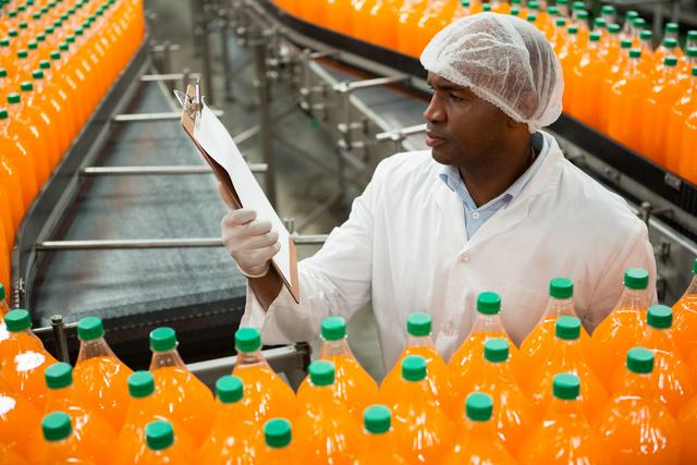 High angle view of male worker reading clipboard while inspecting bottles in juice factory