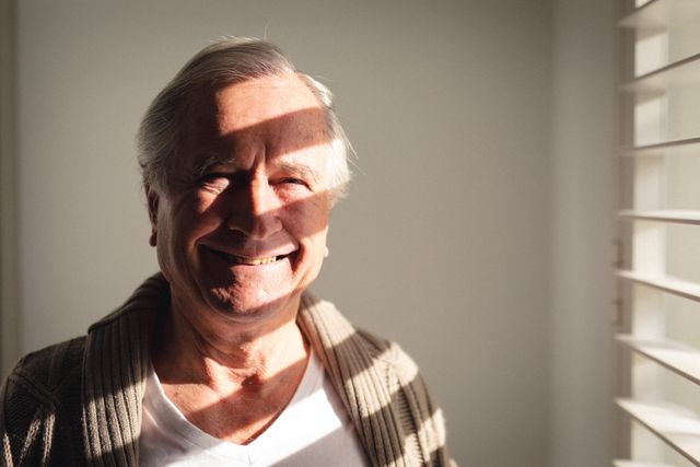 Portrait of caucasian senior man smiling near the window at home - Download Free Stock Photos Pikwizard.com