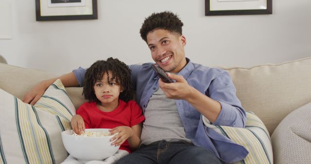 Happy biracial man and his son watching tv together. domestic life, spending time at home.