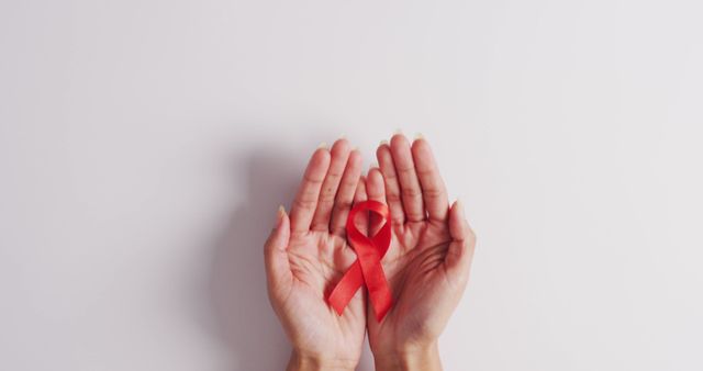 Image of hands of caucasian woman holding red ribbon on white background. medicine, health, cancer awareness concept digitally generated image.