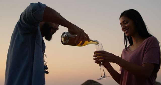 Mixed race Couple having champagne at beach during sunset from