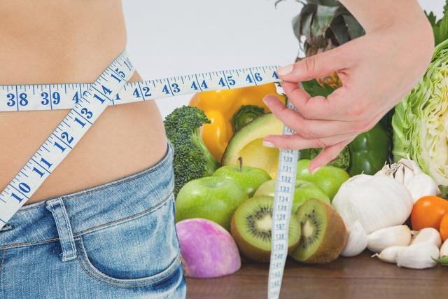 Midsection of woman measuring waist against fruits and vegetables representing weight loss - Download Free Stock Photos Pikwizard.com
