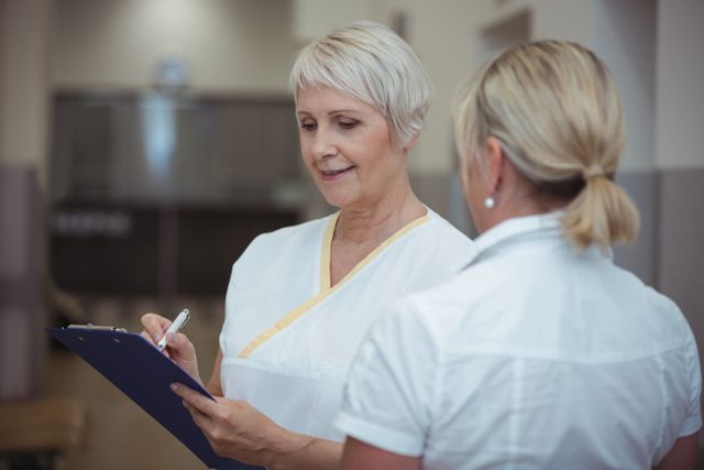 Two nurse having discussion over clipboard in corridor - Download Free Stock Photos Pikwizard.com