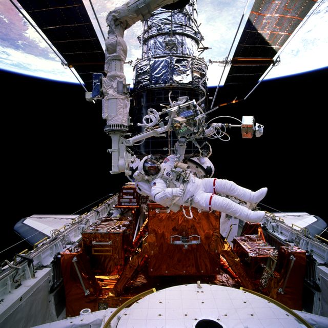 STS082-711-067 (11-21 Feb. 1997) --- Astronaut Gregory J. Harbaugh, mission specialist, floats horizontally in the cargo bay of the Earth-orbiting Space Shuttle Discovery, backdropped against its giant temporary passenger, the Hubble Space Telescope (HST). Harbaugh, sharing this space walking activity with astronaut Joseph R. Tanner (out of frame), is actually recognizable through his helmet visor in the 70mm frame. He is near the Second Axial Carrier (SAC), Axial Scientific Instrument Protection Enclosure (ASIPE). STS-82 marked the first flight of the exit airlock, partially visible at bottom edge of photo.