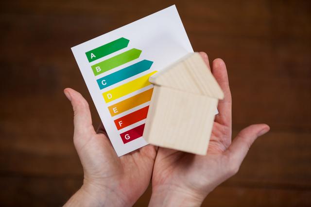 Woman holding miniature house with energy efficiency rating chart - Download Free Stock Photos Pikwizard.com