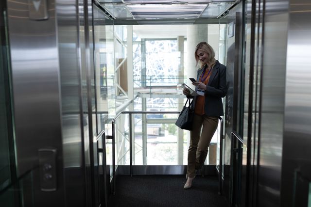 Blonde businesswoman using mobile phone in office elevator - Download Free Stock Photos Pikwizard.com