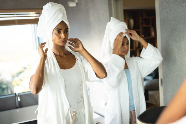 Biracial mother and daughter wearing bathrobes while looking in mirror in bathroom - Download Free Stock Photos Pikwizard.com