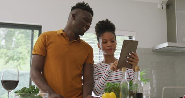 Image of happy african american couple cooking together in kitchen, using tablet. love, relationship, togetherness and spending quality time at home.