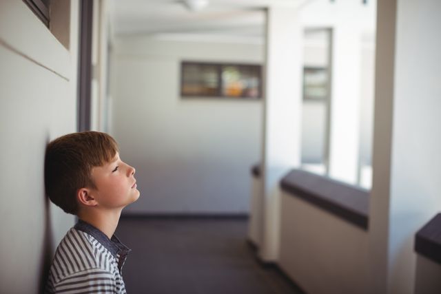 Sad schoolboy leaning head against wall in corridor - Download Free Stock Photos Pikwizard.com