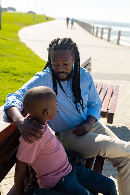 African american father with braided hair talking to son while sitting on bench at promenade - Download Free Stock Photos Pikwizard.com