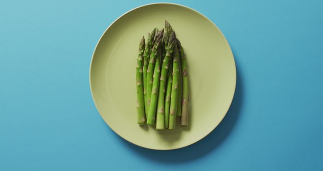 Image of fresh asparagus on green plate over blue background - Download Free Stock Photos Pikwizard.com