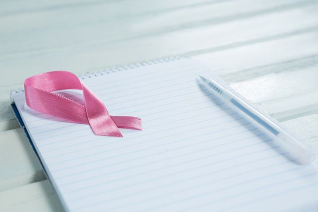 Close-up of pink Breast Cancer Awareness ribbon and spiral notepad with pen - Download Free Stock Photos Pikwizard.com